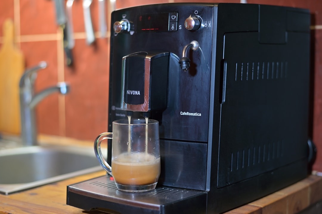 Black coffee machine pours coffee into a glass mug.